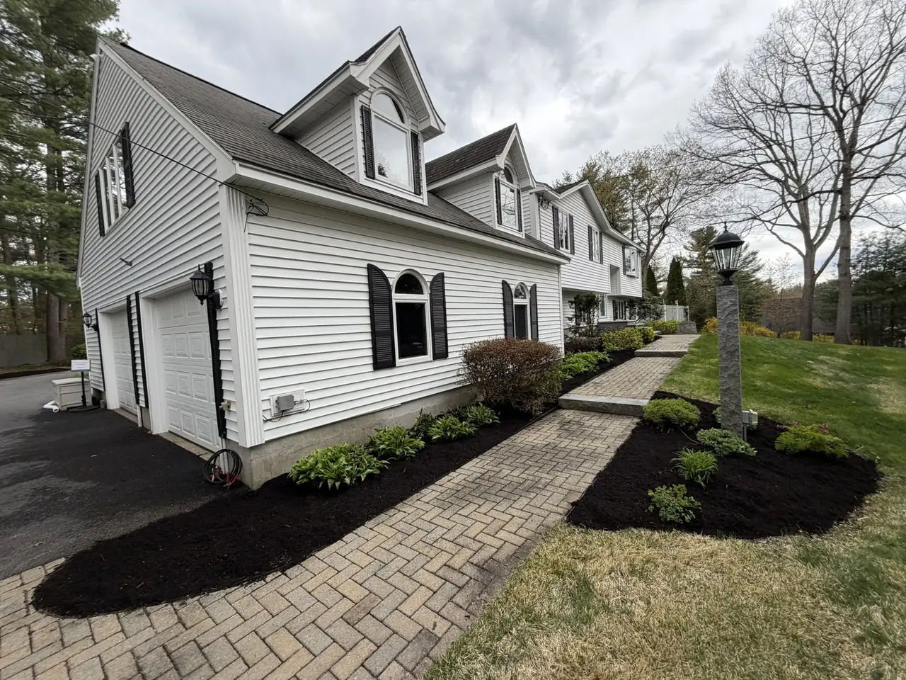 Black mulch beds and paver walkway along a white Cape home in Southern New Hampshire